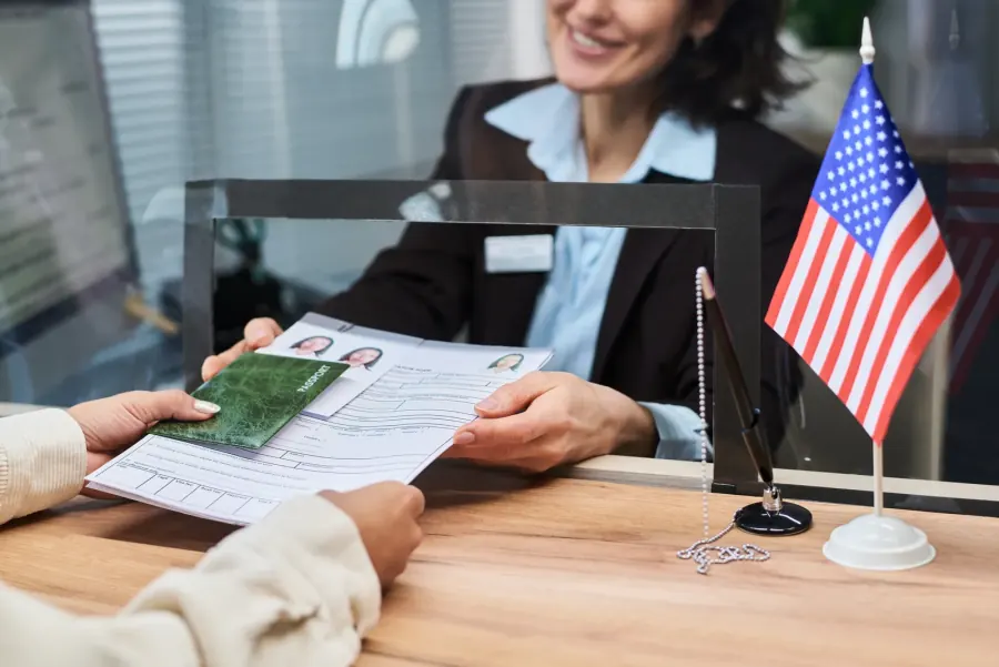 Entrega de passaporte e formulário no balcão do CASV, com a bandeira dos Estados Unidos ao fundo